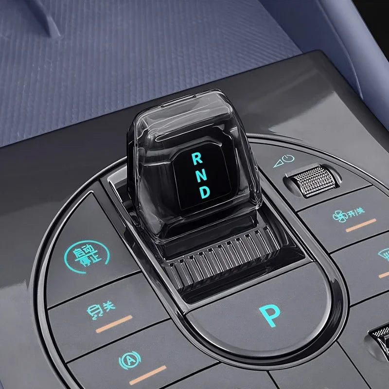Crystal clear transparent gear shifter with glowing cyan RND indicator on a sleek black console.