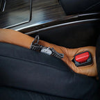 Silver luxury wristwatch with black textured band resting on tan leather car seat upholstery.