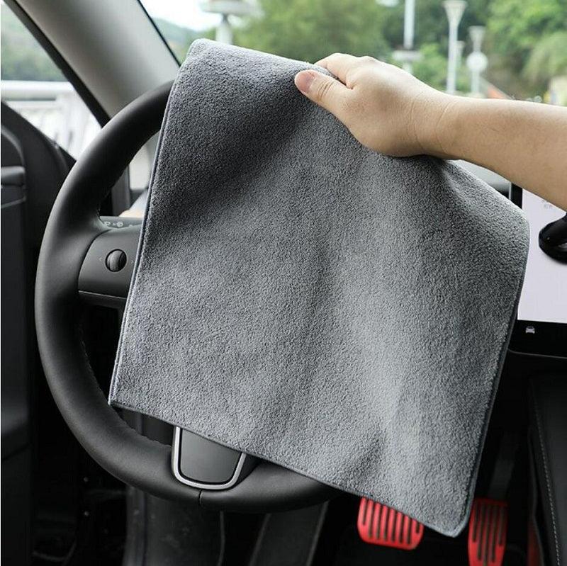 Soft grey microfiber cleaning cloth being used to wipe a black car steering wheel.