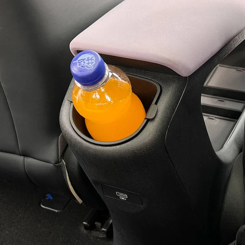 Orange drink bottle in a black matte plastic car cup holder with a grey armrest.