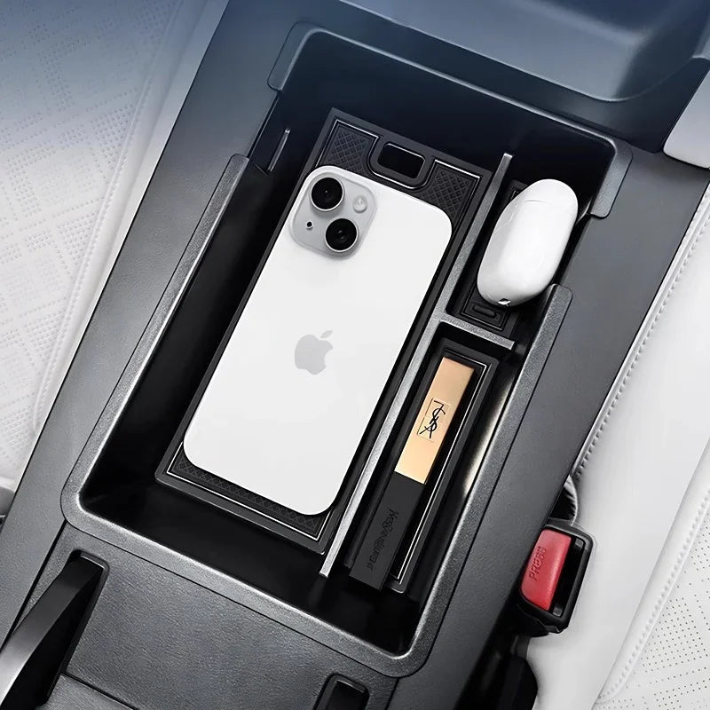 Black carbon fiber center console organizer for BYD featuring a white iPhone and wireless earbuds.