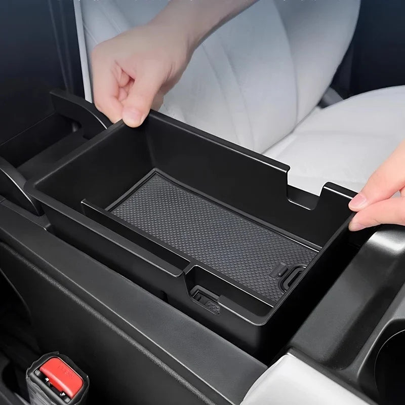 Hand installing a matte black center console organizer tray with a non-slip rubber mat.