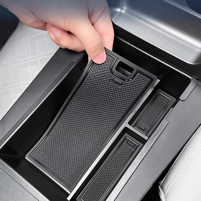 Hand placing a black textured silicone tray into a car center console compartment.