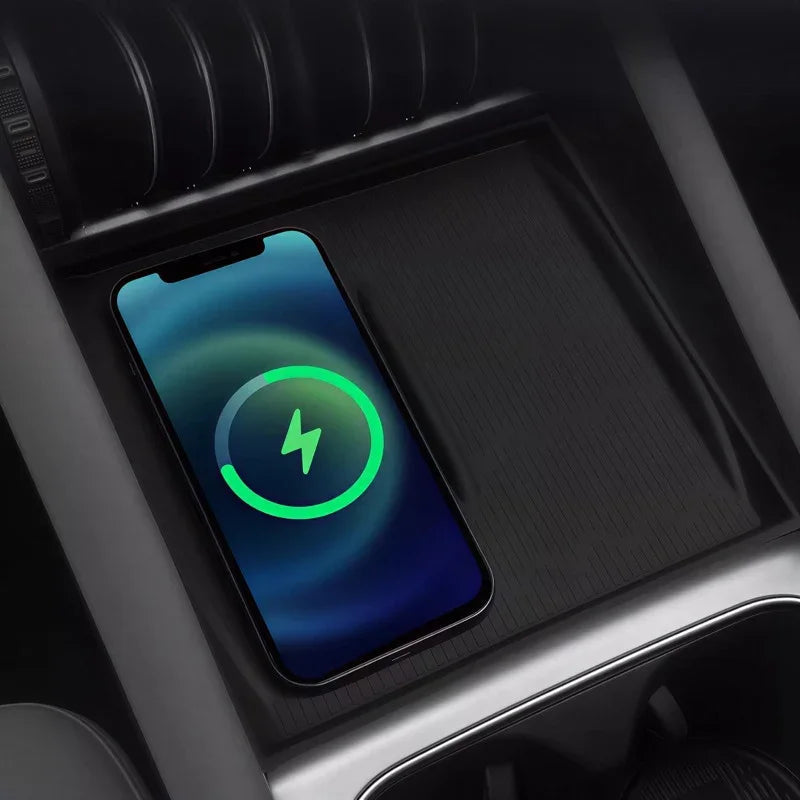 Black textured wireless charging pad with a smartphone charging in a car center console.