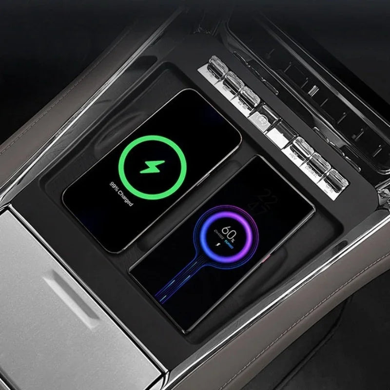 Two smartphones charging on a sleek black wireless charging pad inside a car console.