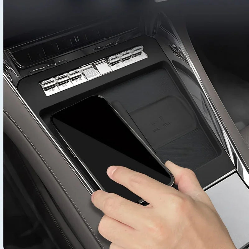 Black wireless charging pad in a car center console with a smartphone being placed on it.