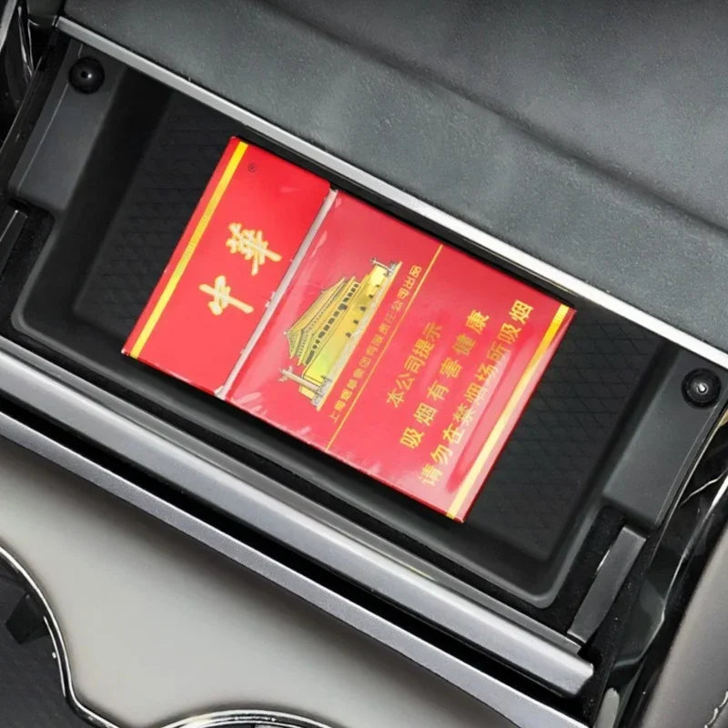 Red and gold rectangular box placed inside a black car center console storage compartment.