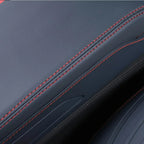 Close-up of dark grey leather car interior upholstery with contrasting red double stitching.