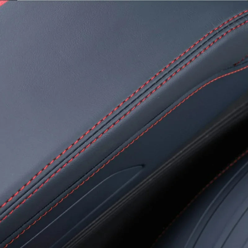 Close-up of dark grey leather car interior upholstery with contrasting red double stitching.