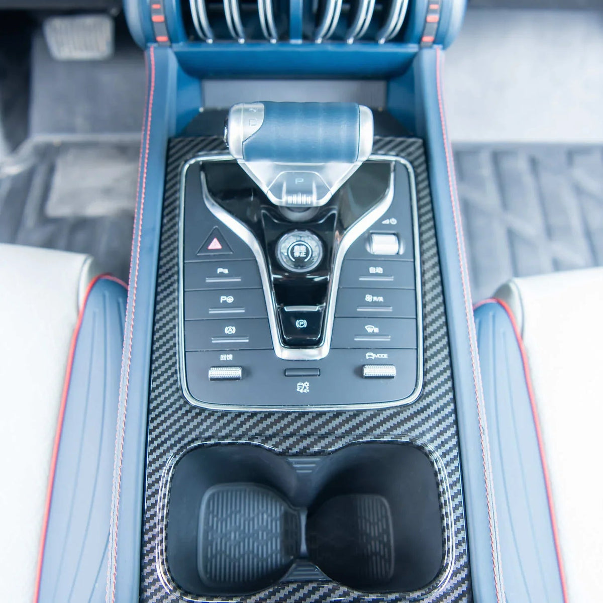 Blue leather center console with carbon fiber trim and red stitching for a luxury car interior.