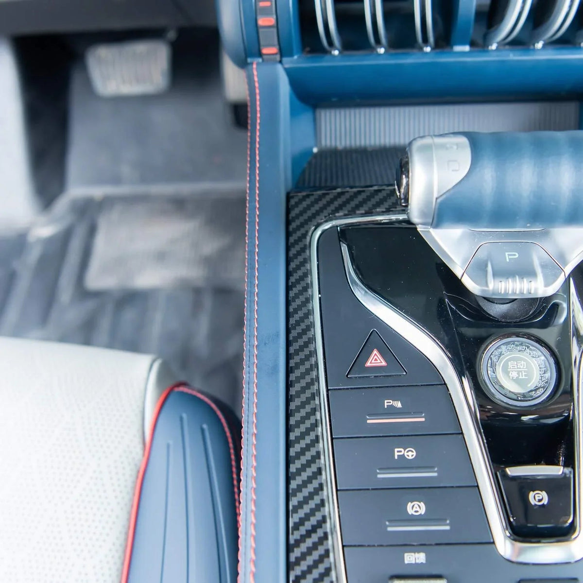 Close-up of a blue leather car interior with carbon fiber trim and red stitching details.