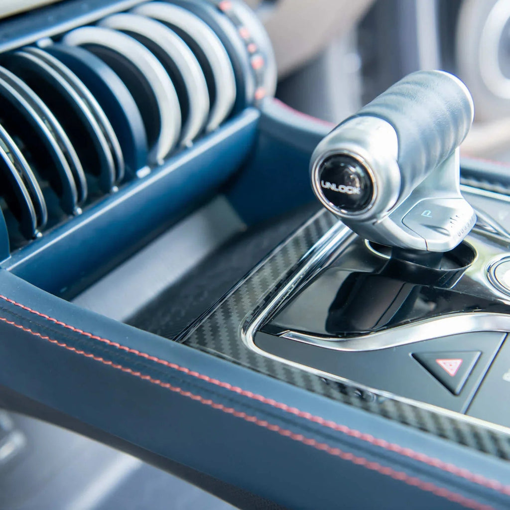Close-up of a luxury car interior featuring a carbon fiber center console and blue leather with red stitching.