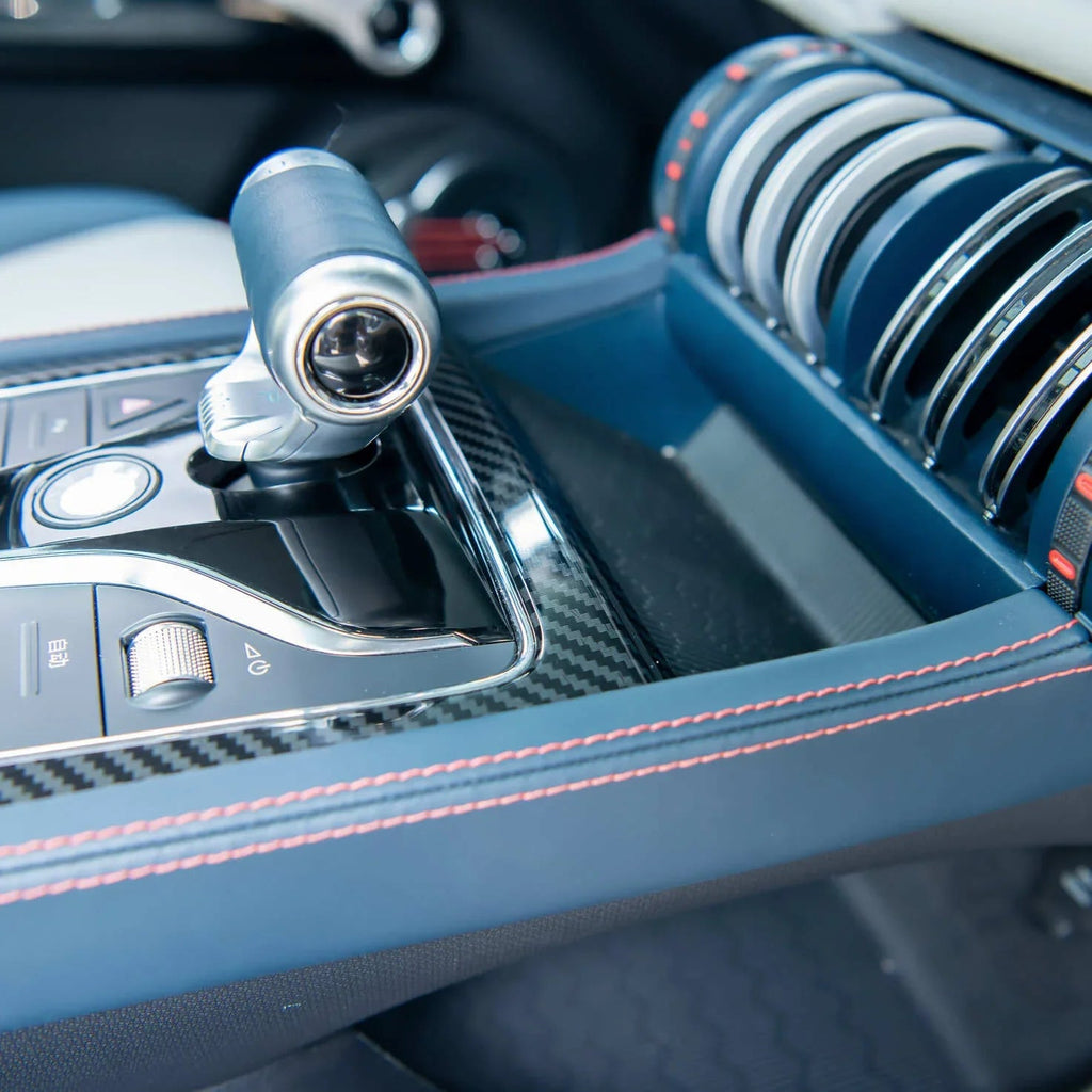 Blue leather car center console with carbon fiber accents and orange contrast stitching.