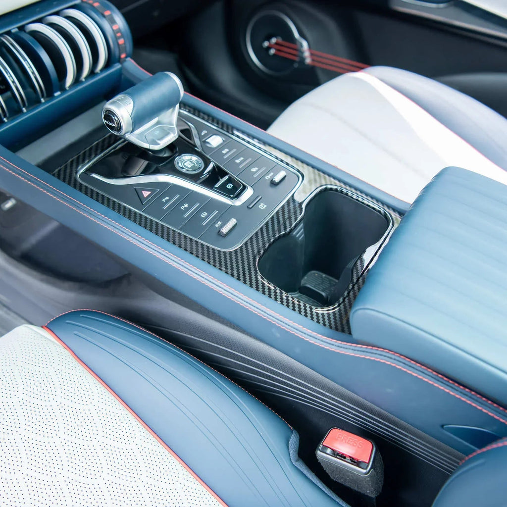 Close-up of a blue luxury car center console with carbon fiber trim and red stitching.