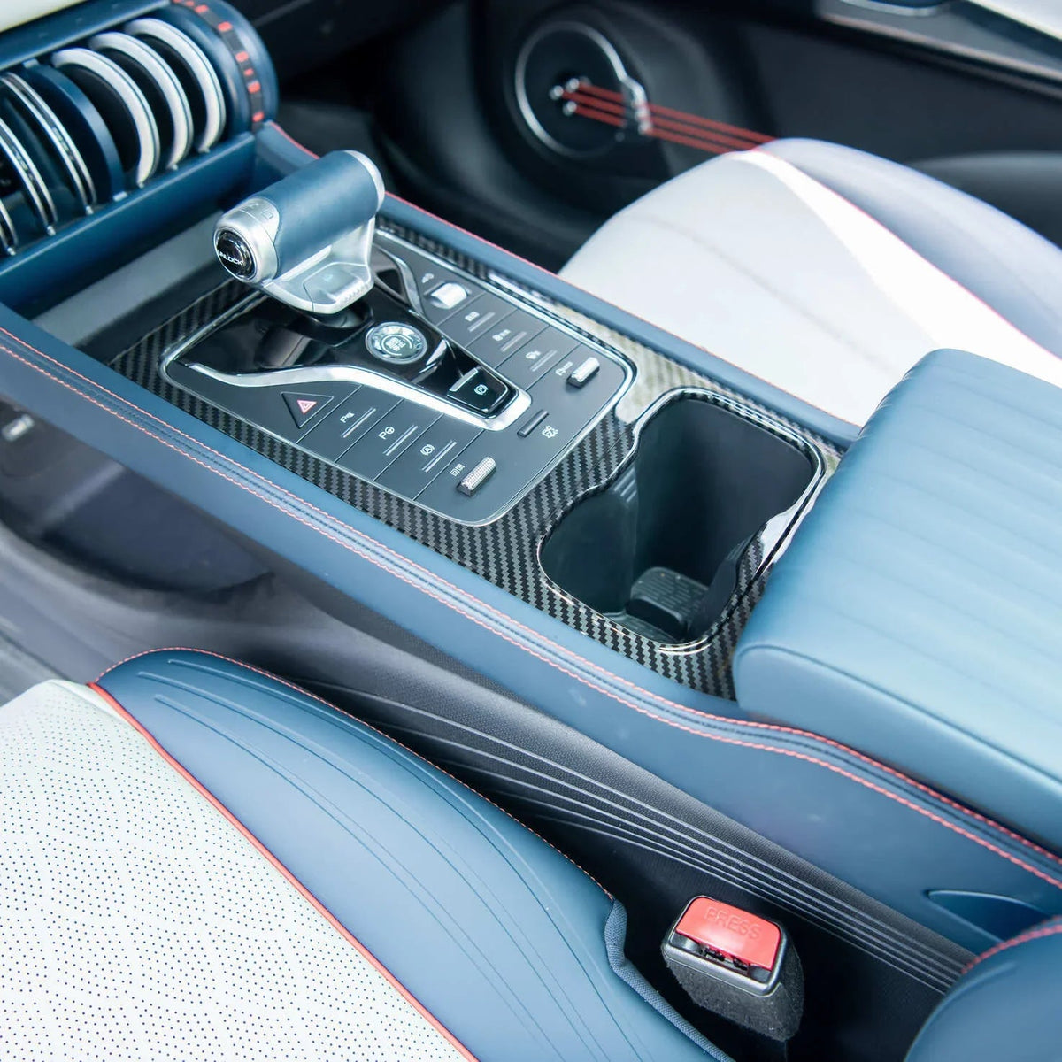 Close-up of a blue luxury car center console with carbon fiber trim and red stitching.