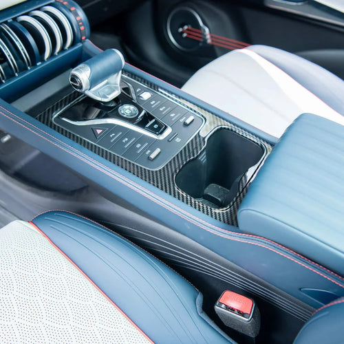 Close-up of a blue luxury car center console with carbon fiber trim and red stitching.