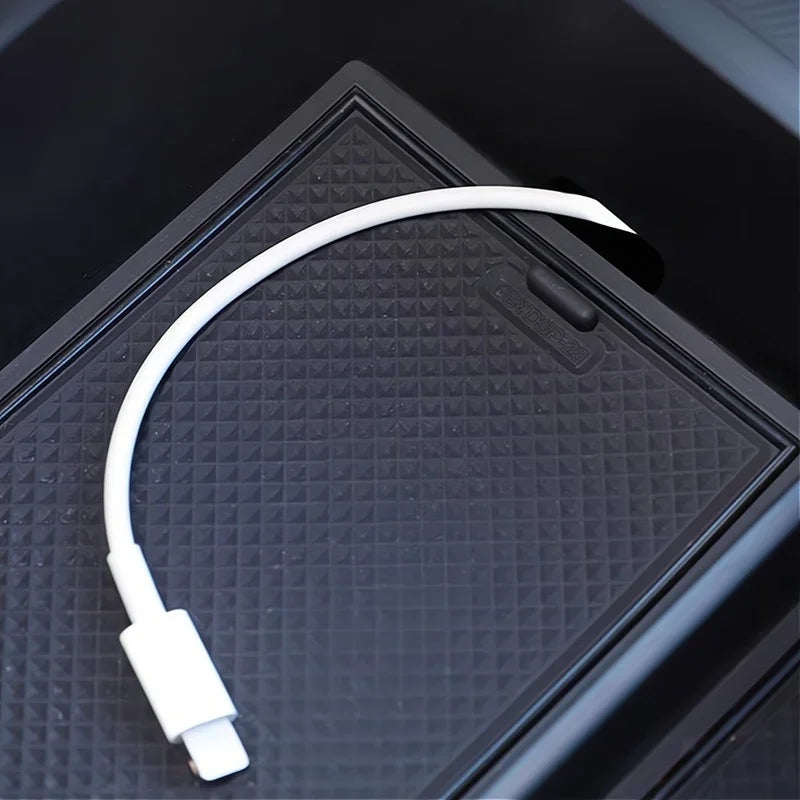 White USB-C charging cable resting on a textured black protective car console tray.