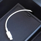 White USB-C charging cable resting on a textured black protective car console tray.