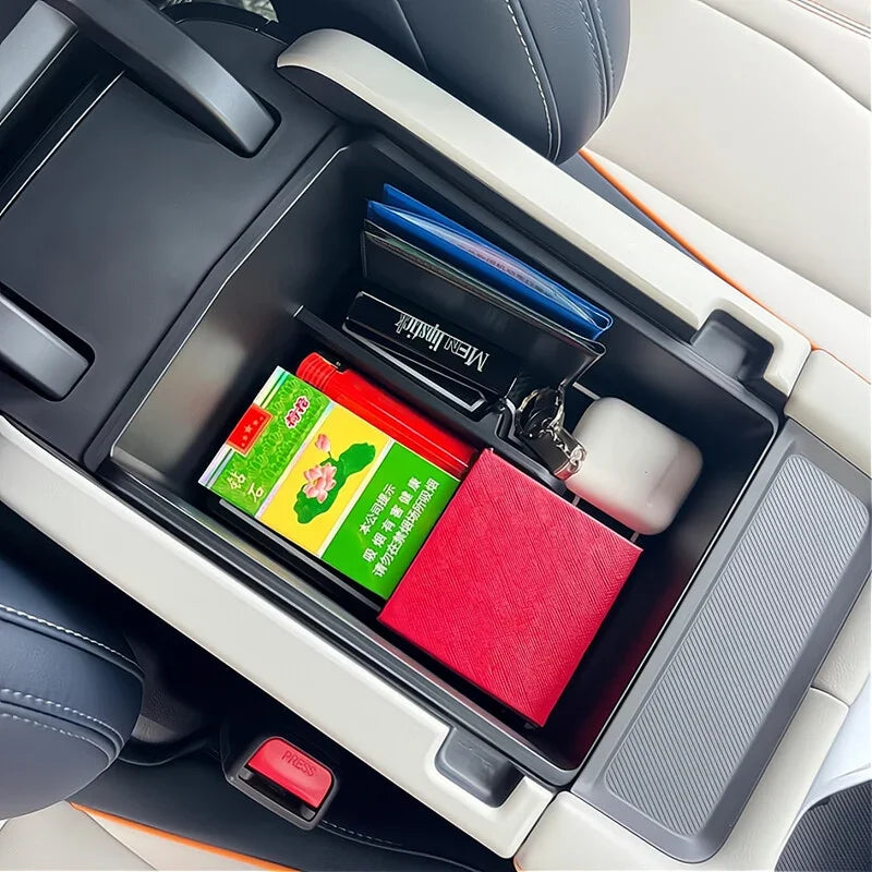 Organized black car center console storage compartment containing a red notebook and small essentials.