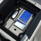 Beige center console organizer tray with a key fob and documents in a car interior.