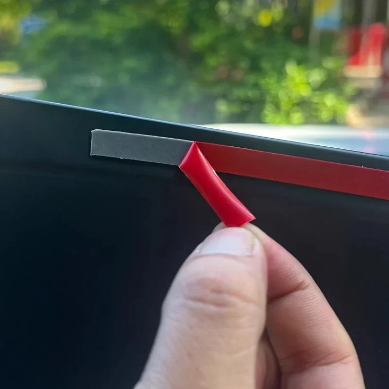 Peeling back a red protective film from a black car trim accessory to reveal the surface.