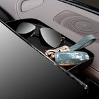 Black leather car center console organizer tray holding dark sunglasses and a blue quilted accessory.
