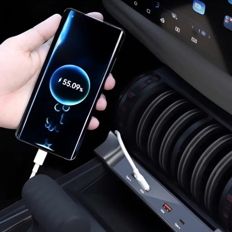 A hand holding a smartphone being charged via a white USB-C cable connected to a car's center console.