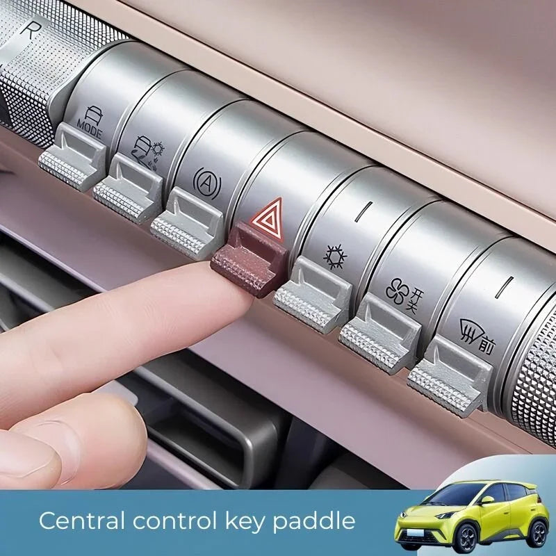 A finger pressing a silver metal central control key paddle with a red triangle icon in a car interior.