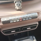 A small white bear figurine sitting on a beige car dashboard near the silver gear selection buttons.
