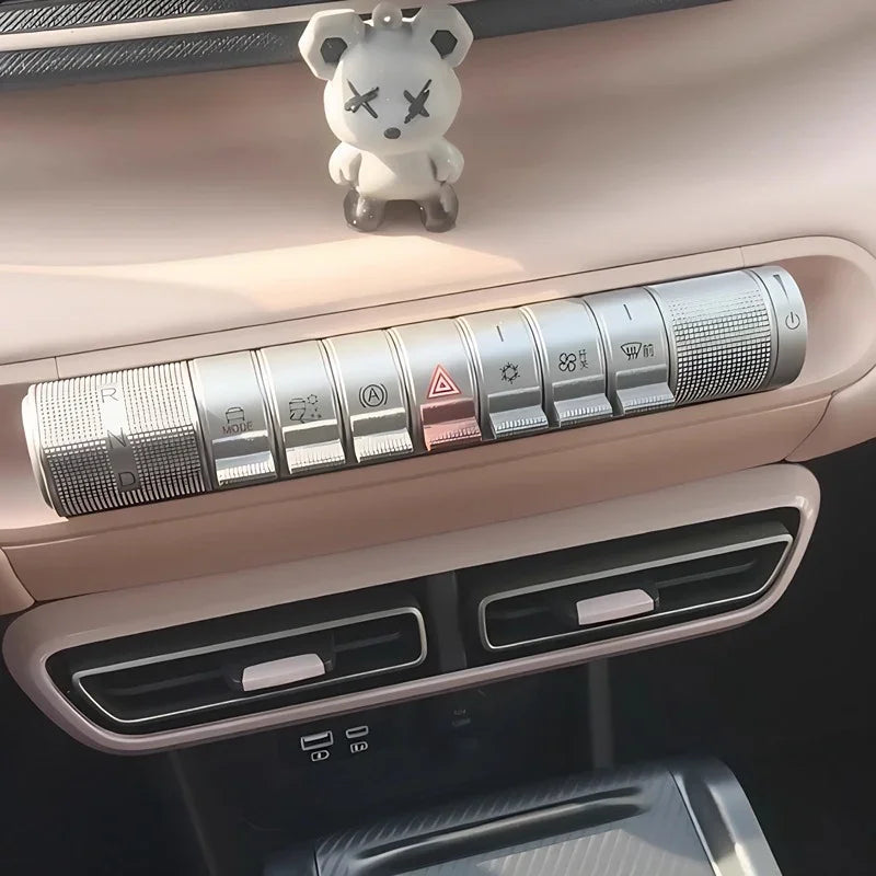 A small white bear figurine sitting on a beige car dashboard near the silver gear selection buttons.
