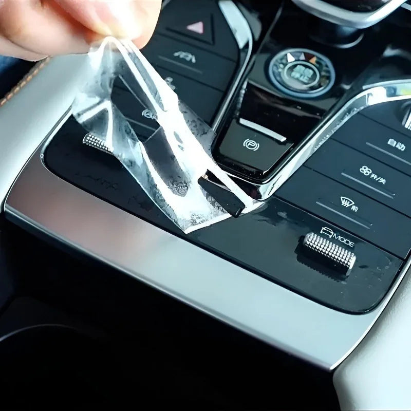 Transparent protective film being applied to a black car center console control panel.