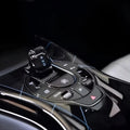 Glossy black carbon fiber texture center console with illuminated gear shifter and control buttons.