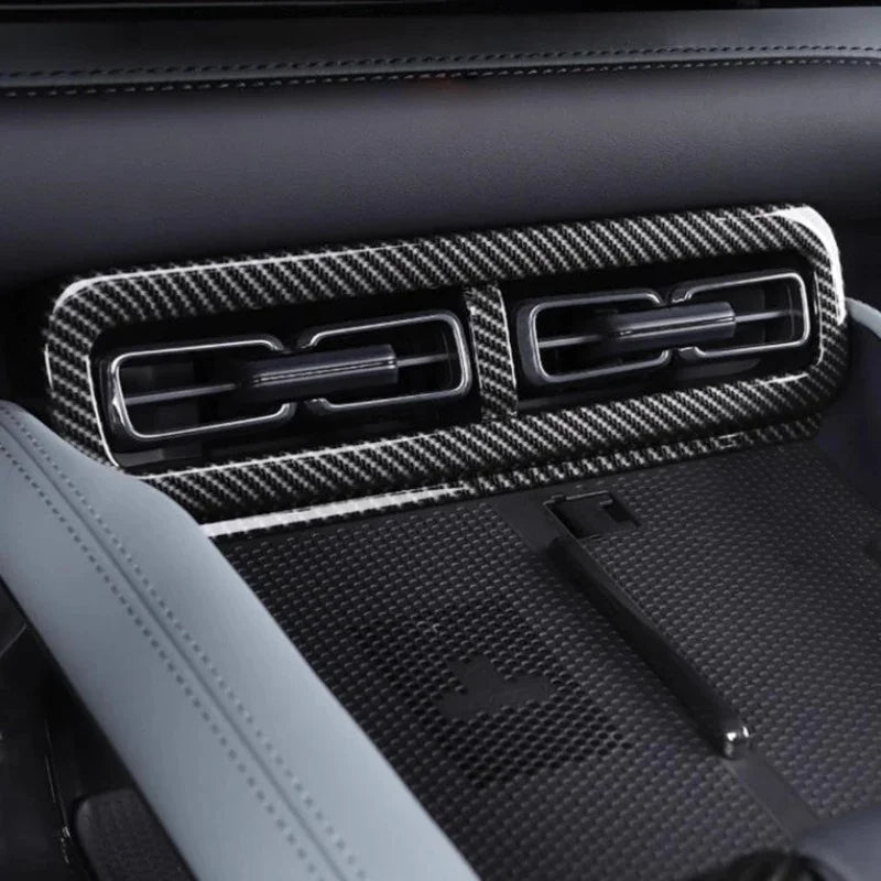Premium black carbon fiber trim panel covering automotive air vents and dashboard console.
