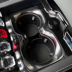 Close-up of a glossy black car center console with dual cup holders and a textured finish.