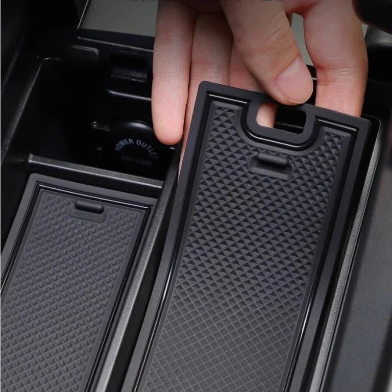 Hand inserting a black textured rubber center console organizer tray for BYD car interior.