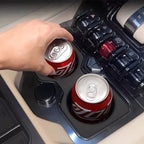 Two red aluminum beverage cans placed in a black sleek car center console cup holder.