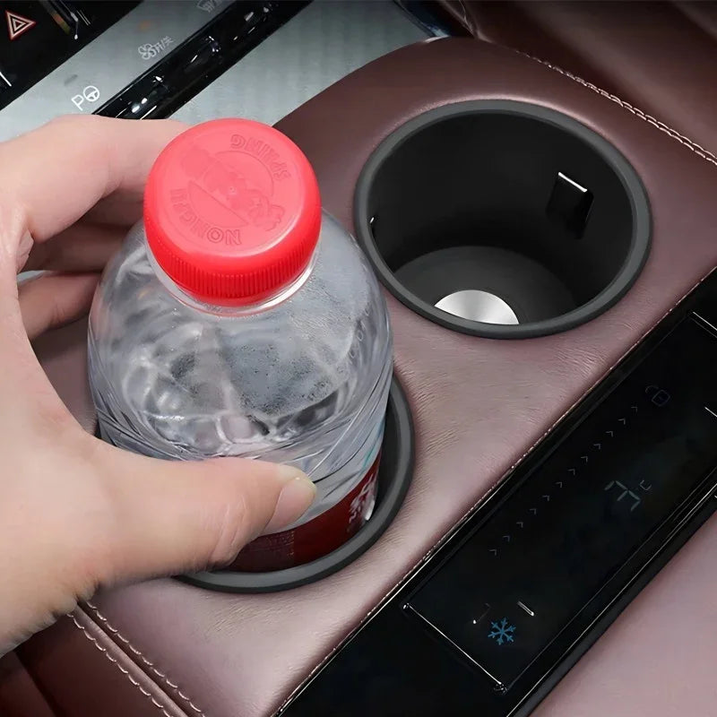 A hand placing a clear water bottle into a black matte car cup holder integrated into brown leather interior.