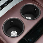Two black circular cup holders embedded in premium burgundy leather car center console.
