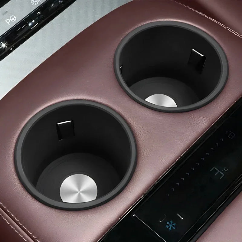 Two black circular cup holders embedded in premium burgundy leather car center console.