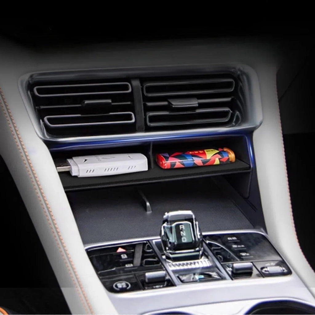 Black leather car center console organizer tray holding a white USB drive and colorful accessory.