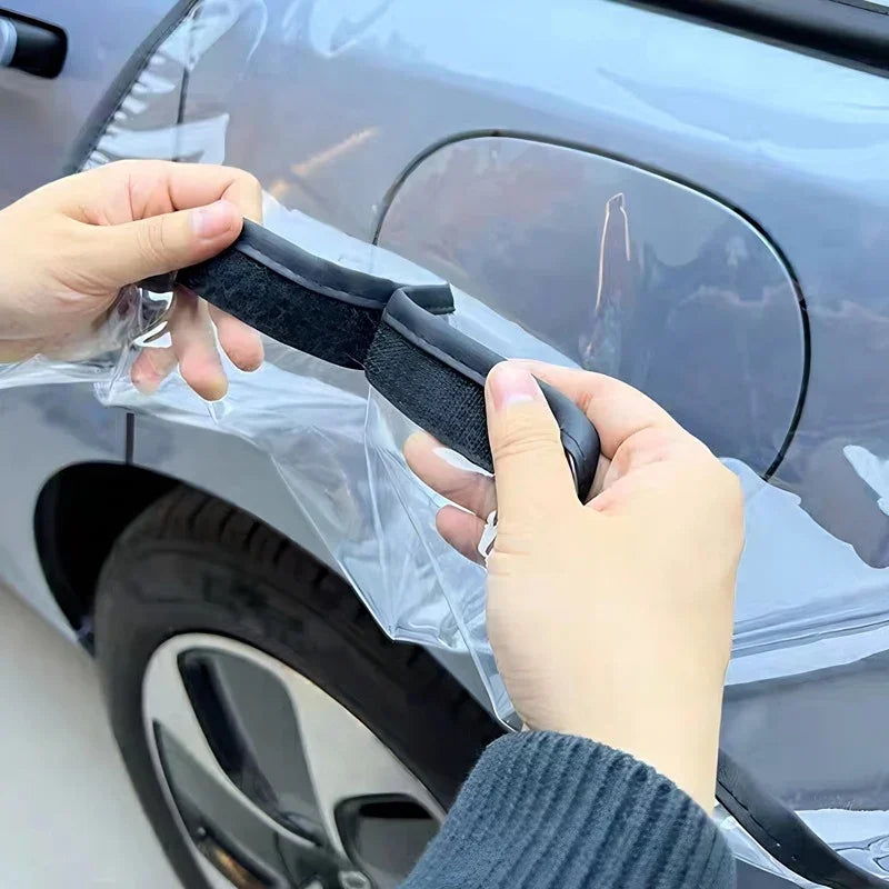 Hands installing a clear waterproof car cover with black Velcro fastening strips on a grey vehicle.