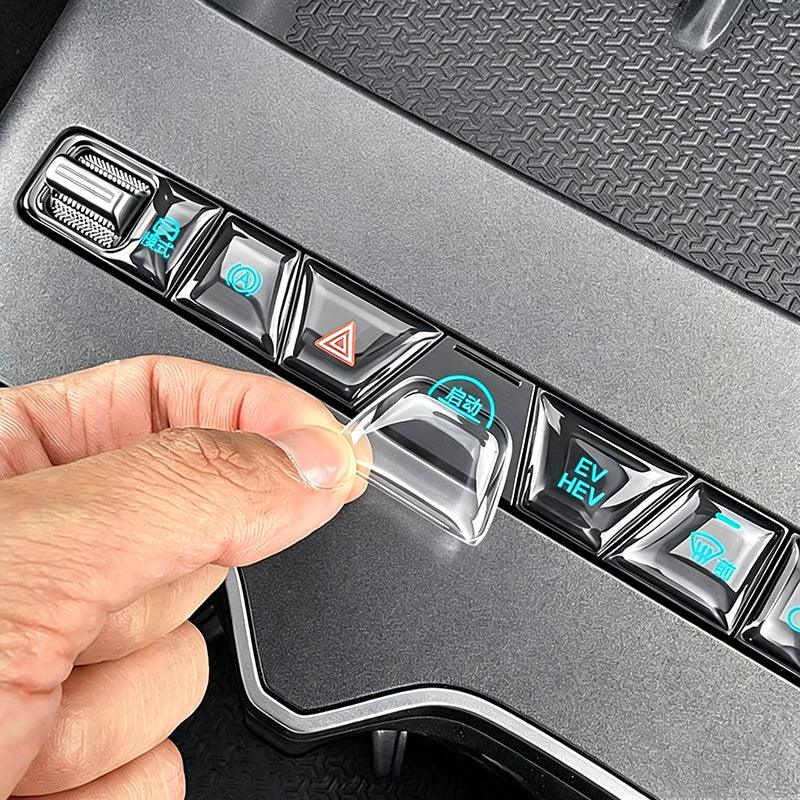 Hand applying a transparent TPU protective film to a BYD car center console button.