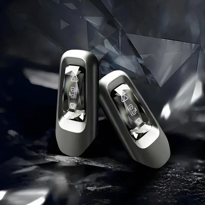 Two sleek silver BYD car remote key fobs with polished chrome accents on a dark crystalline background.