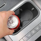 Hand placing a red aluminum soda can into a black matte plastic car center console cup holder.