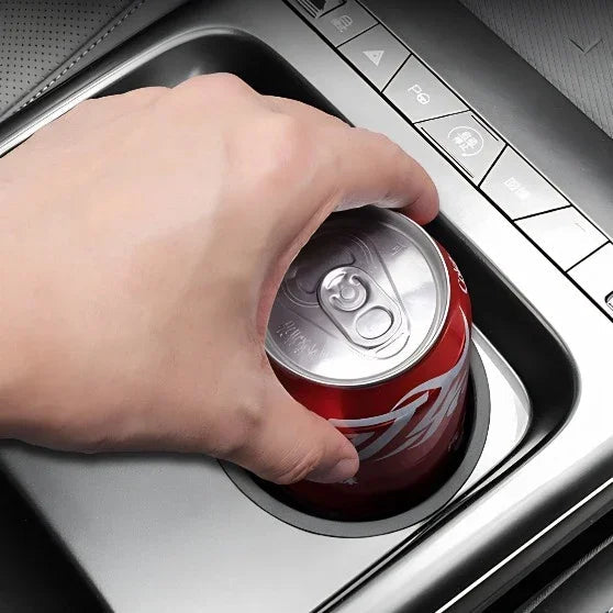 A hand placing a red aluminum soda can into a sleek silver metallic car cup holder.