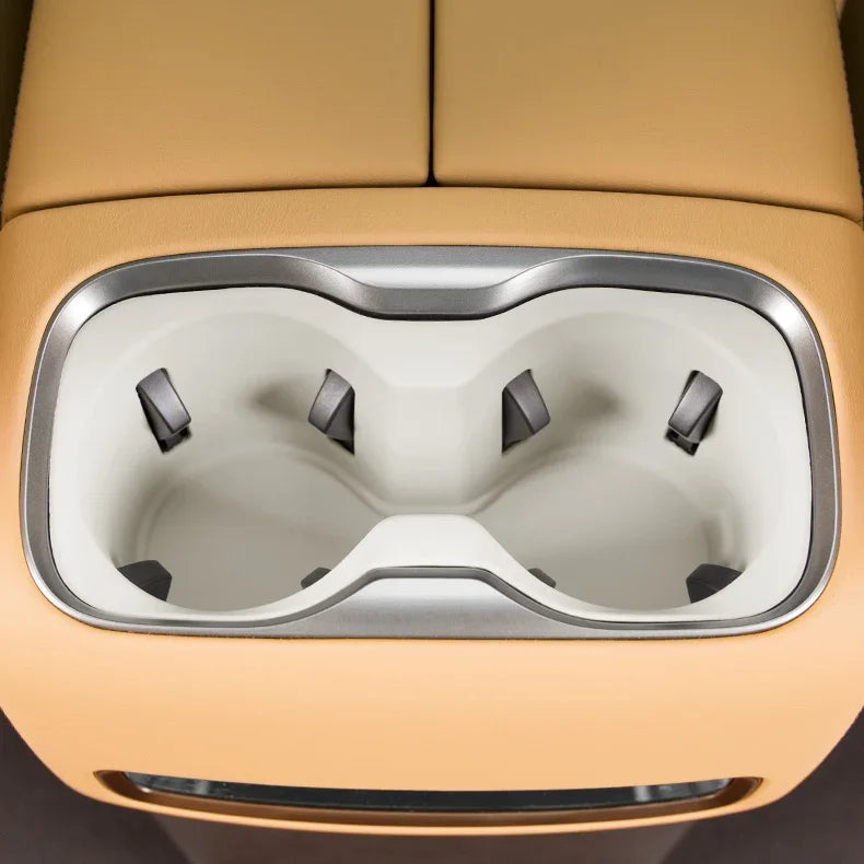 Dual beige integrated cup holders with silver trim in a tan leather car center console.