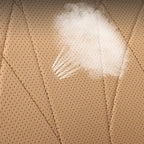 Spilled white liquid on tan perforated leather car seat upholstery.
