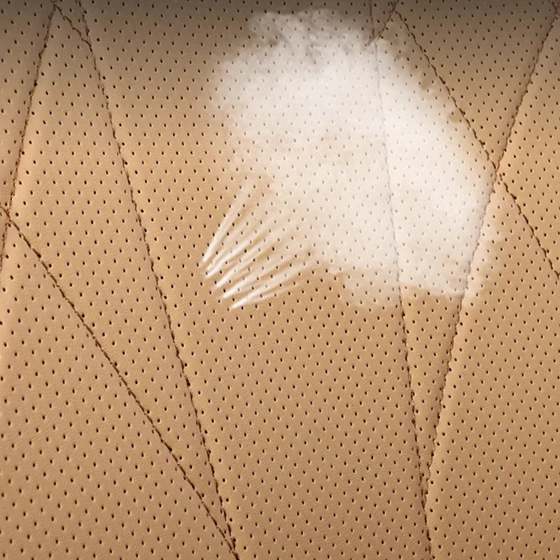 Spilled white liquid on tan perforated leather car seat upholstery.
