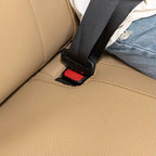 Close-up of a black seatbelt buckled into a perforated tan leather car seat.