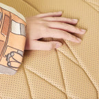Close-up of a hand touching tan perforated faux leather car seat cover with diamond stitching.
